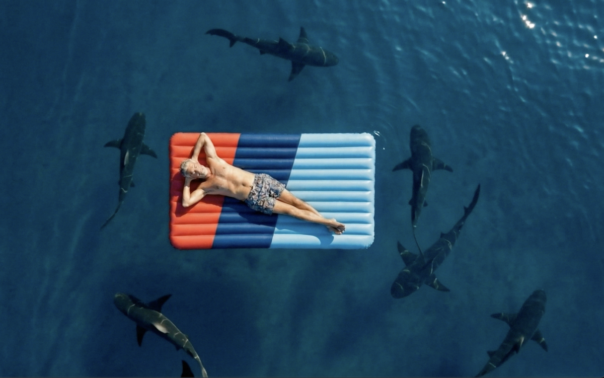 Man relaxing on a CMCM-branded pool float in a sea full of sharks.