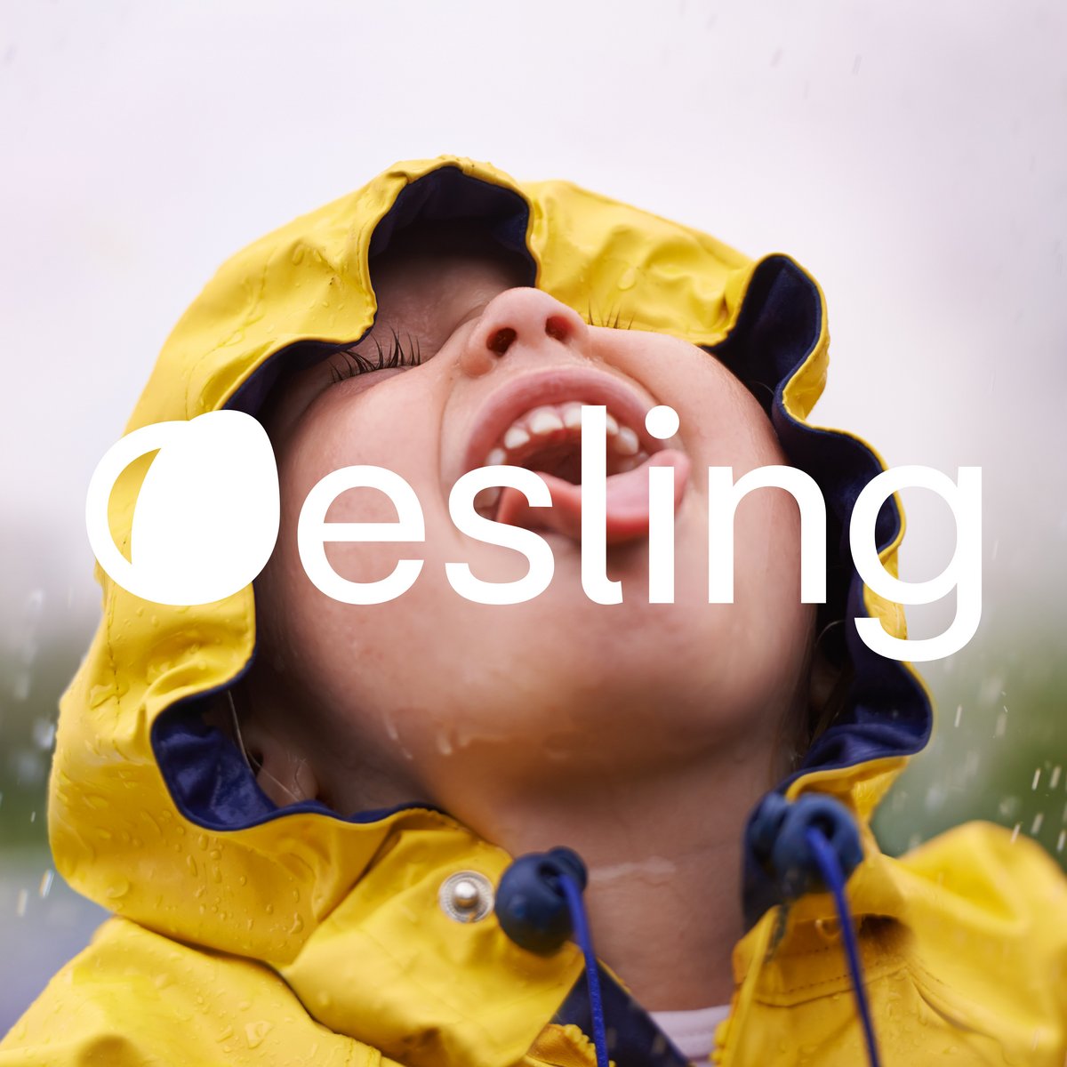 A toddler in the rain with a yellow rain jacket and sticking out his tongue